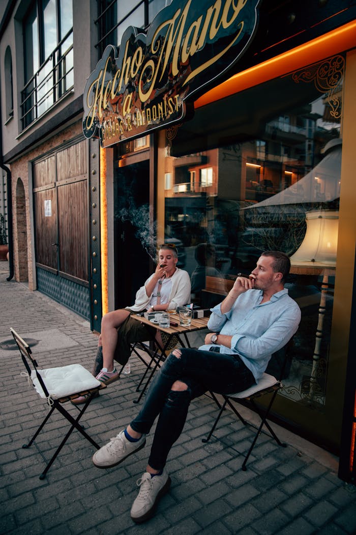 Two men enjoying cigars outside a stylish store on a vibrant city sidewalk.