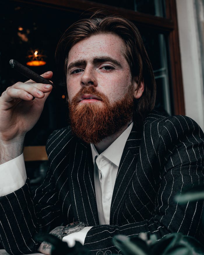 Portrait of a redhead man in a pinstripe suit smoking a cigar indoors.